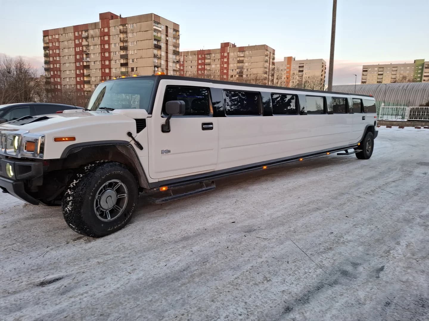 Długa, biała limuzyna Hummer zaparkowana na ośnieżonym parkingu przed blokami.