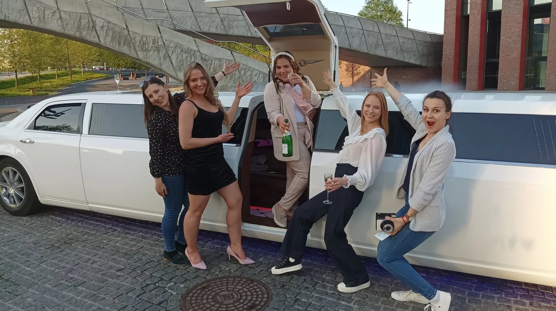 Grupa przyjaciółek świętująca przy białej limuzynie z otwartymi drzwiami w słoneczny dzień.