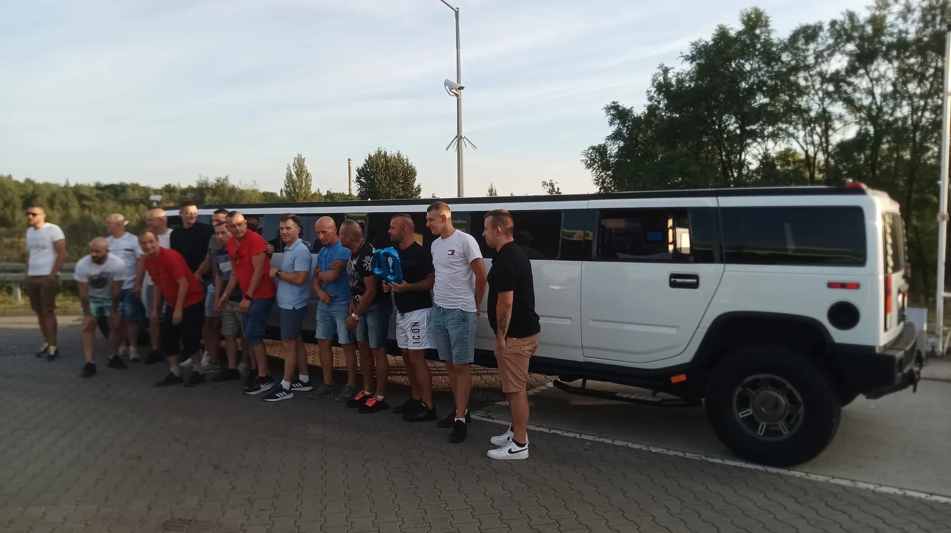 Grupa mężczyzn stojąca obok długiej, białej limuzyny typu Hummer na parkingu.